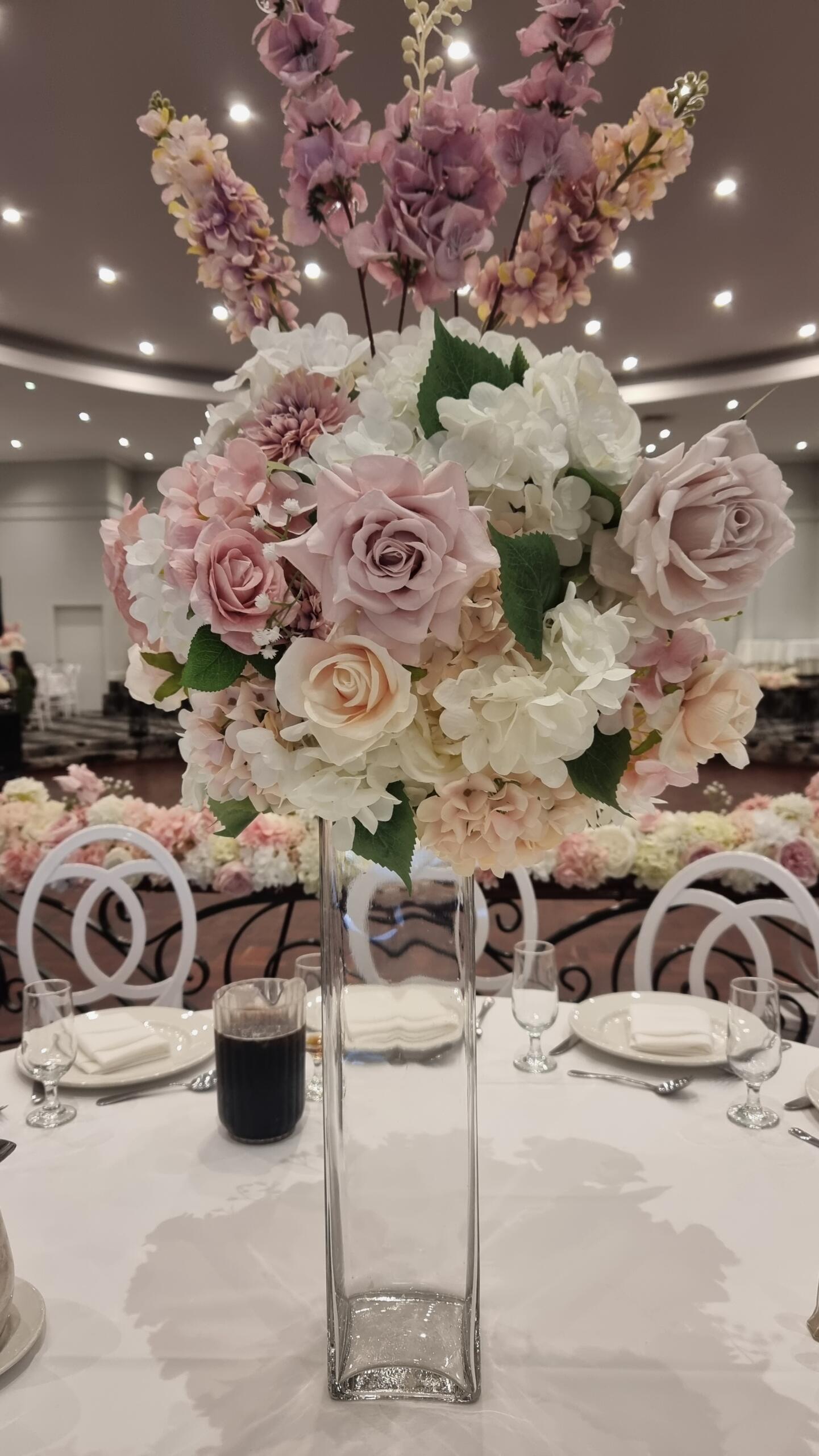 Tall blush pink and white wedding floral centrepiece in a clear glass vase on a reception table