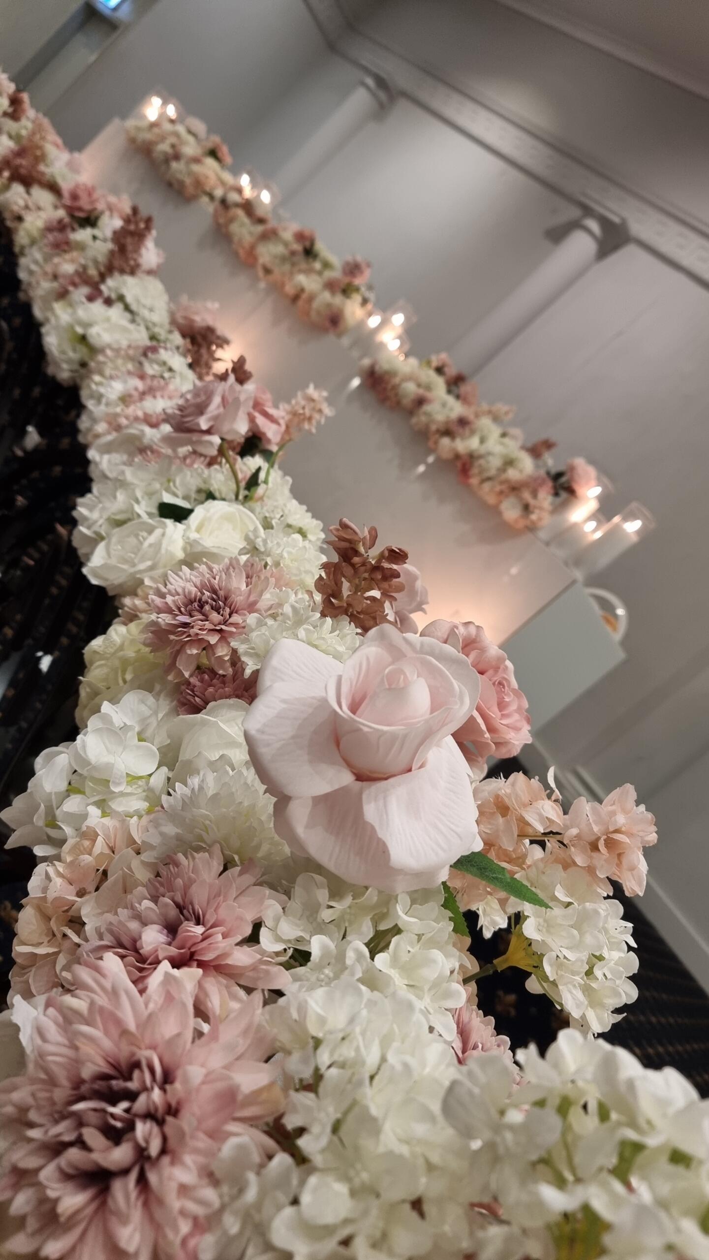 Close-up of blush pink and white wedding floral table arrangements with soft candlelight backdrop